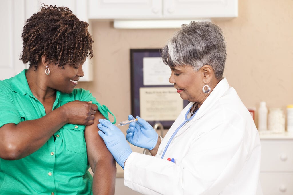 Doctor or nurse gives flu vaccine to patient at clinic.